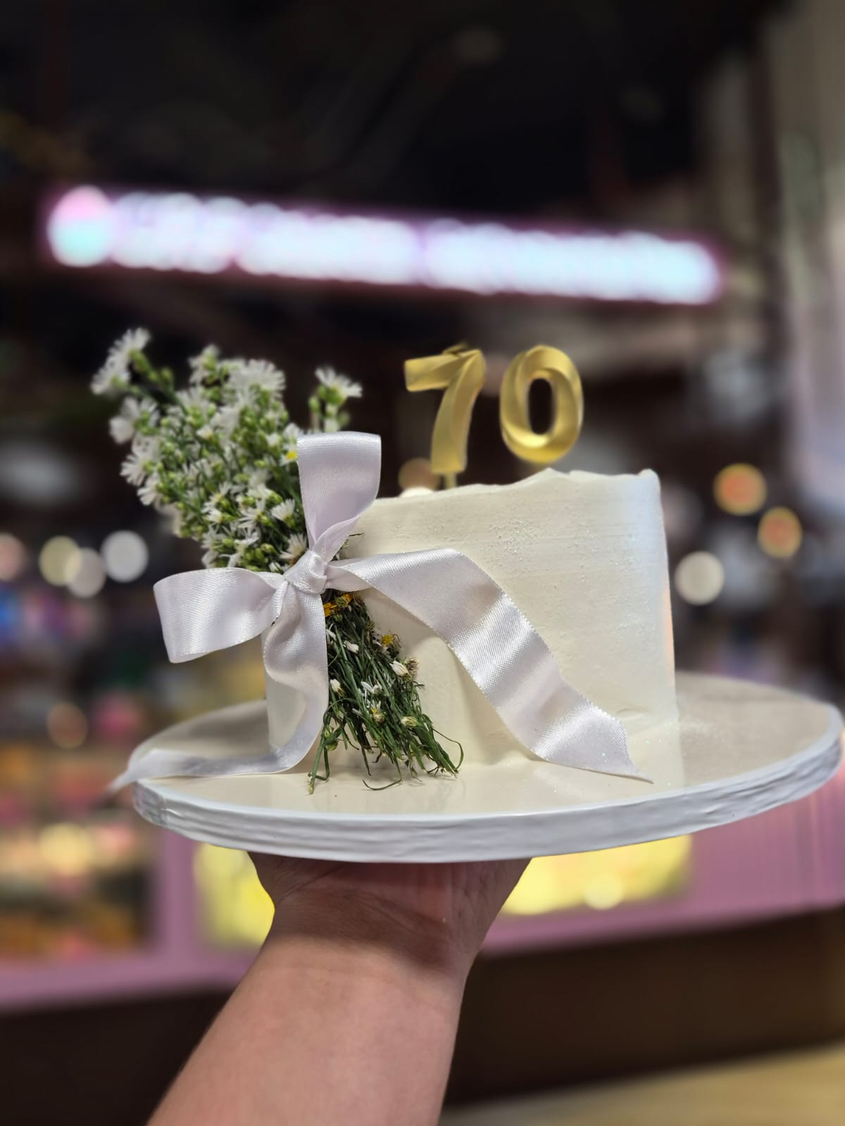 Torta blanca con flores, lazo blanco y número 70 dorado