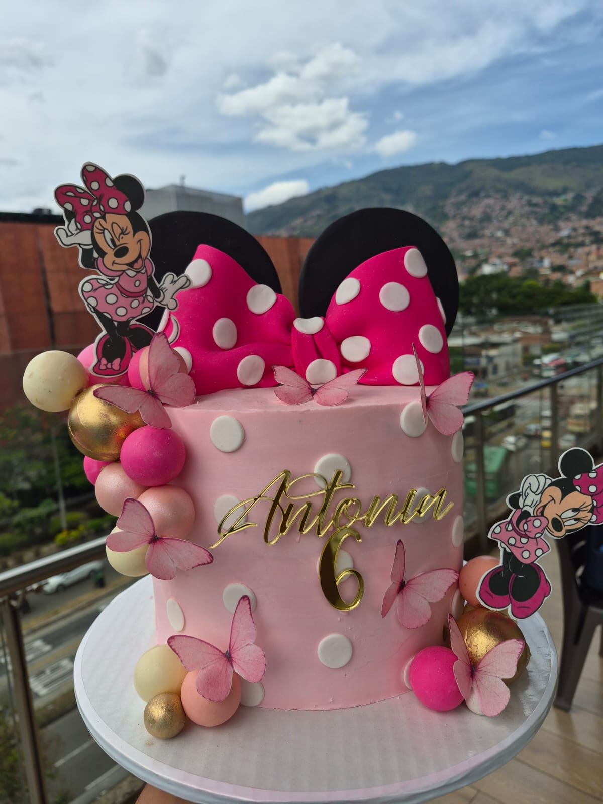 Torta rosada de Minnie con un gran moño, mariposas y decoración dorada